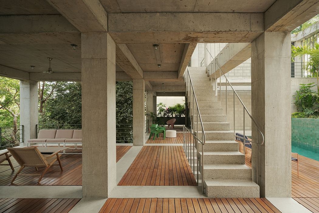 Modern home interior with concrete pillars, wooden flooring, stairs, and patio furniture.