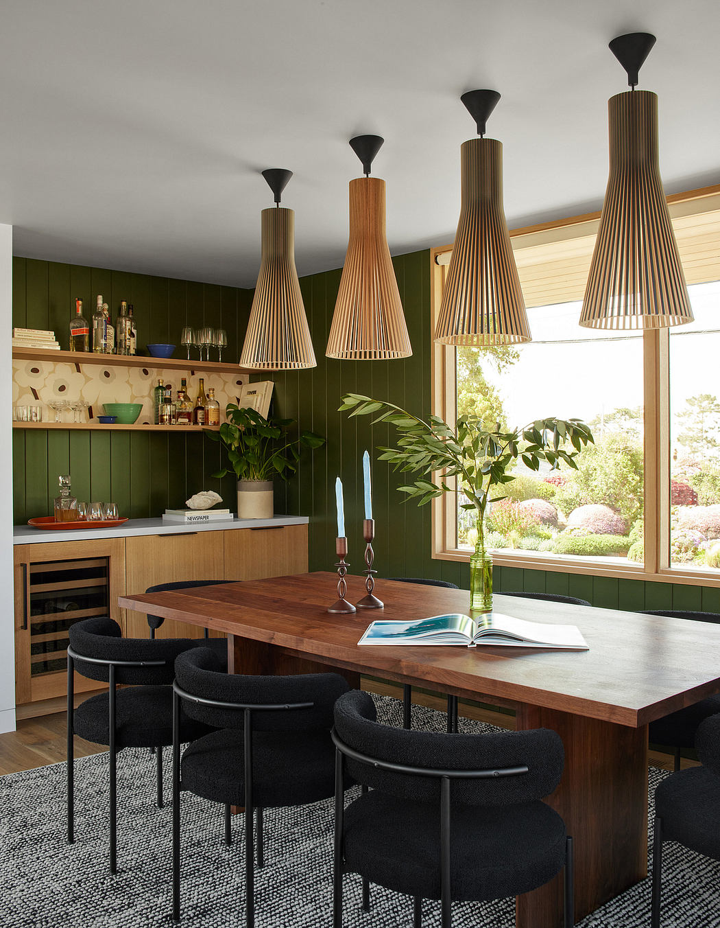 Modern dining room with wooden table, black chairs, pendant lights, and green walls