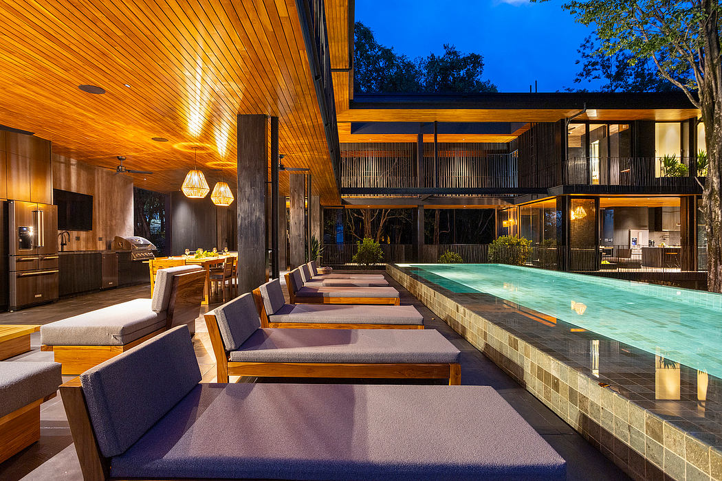 Modern outdoor pool area with loungers and a view of a house at dusk.