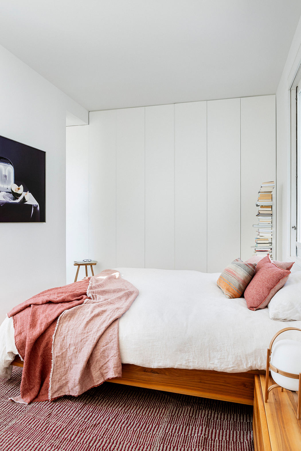 Minimalist bedroom with white walls, a wooden bed, and a pink throw blanket
