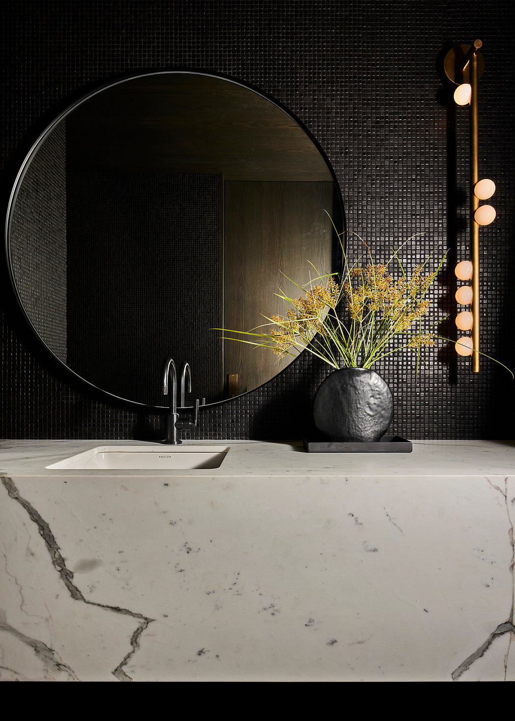 Modern bathroom with a circular mirror, marble countertop, and vertical light fixture.
