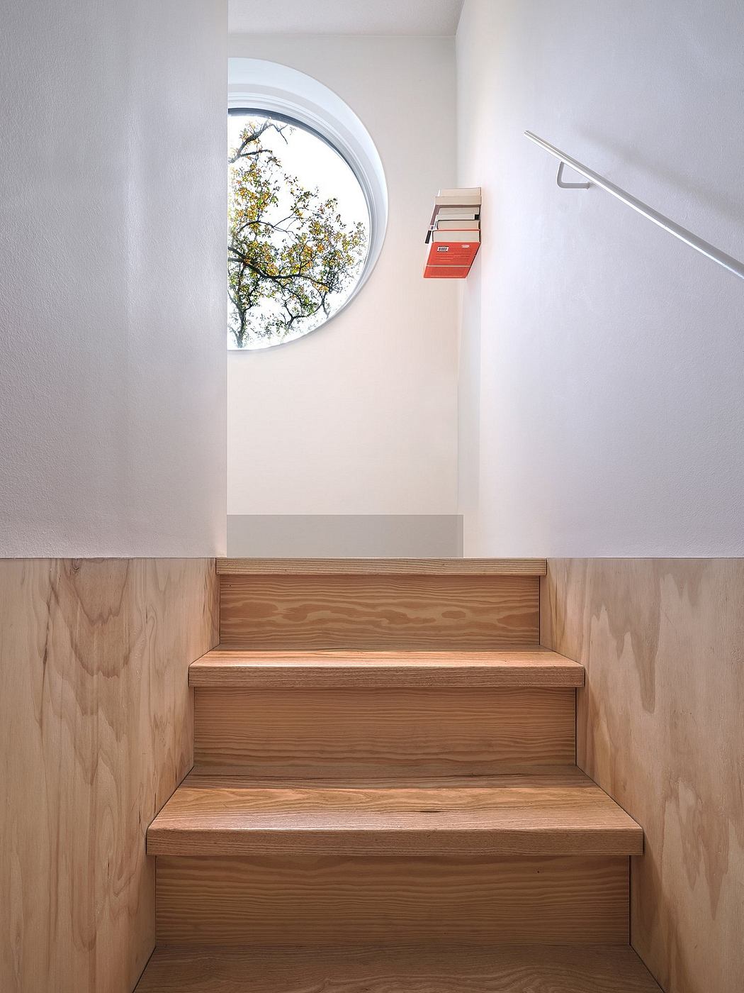 Minimalist stairway with wooden steps, white walls, round window, and a
