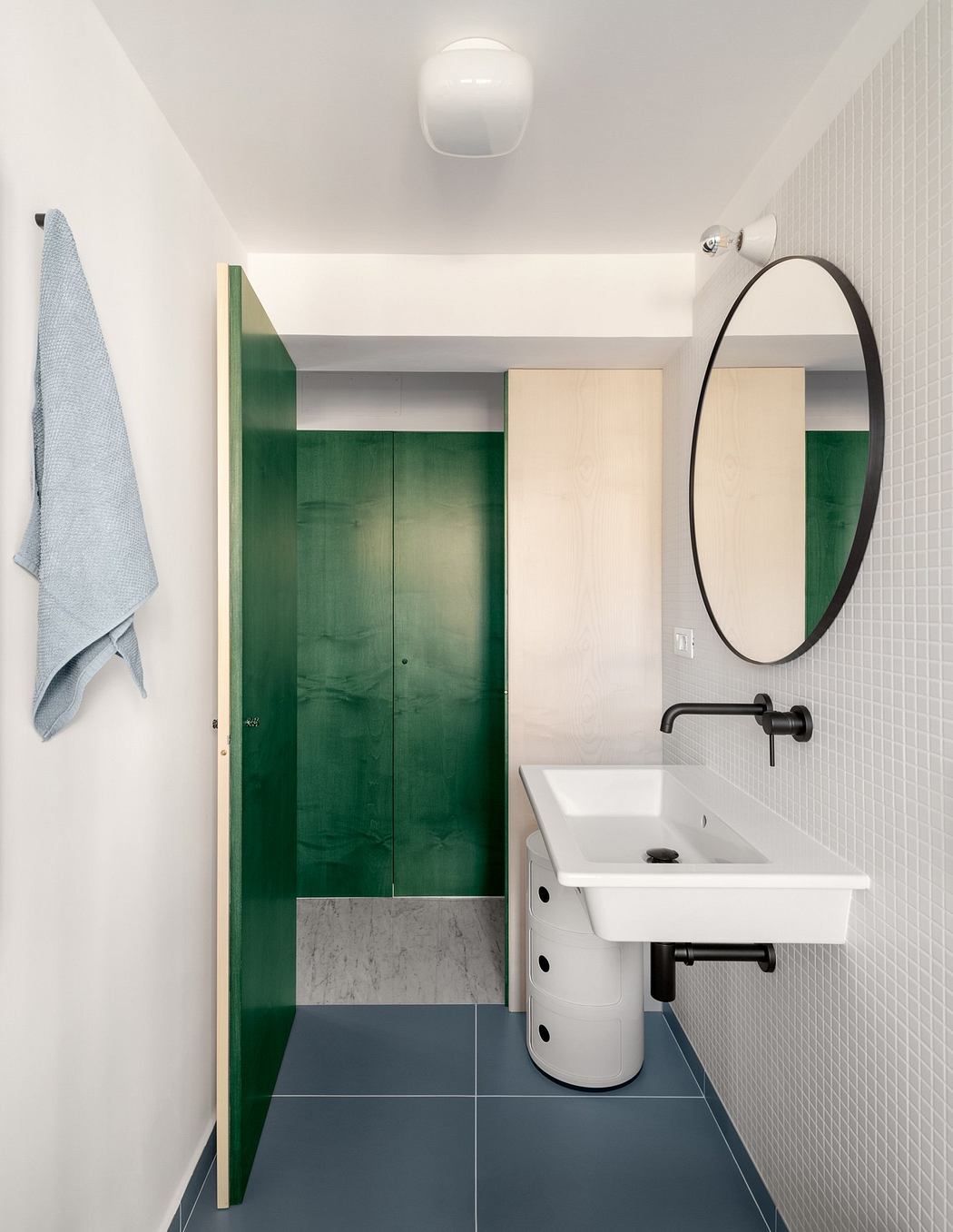 Sleek bathroom with green door, oval mirror, and blue floor tiles.