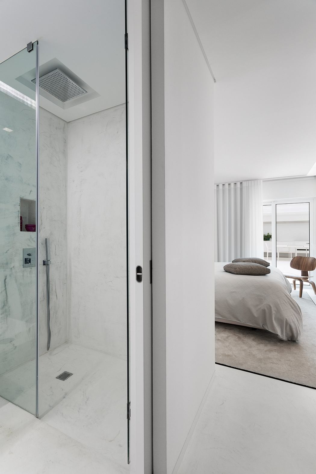 Minimalist white bedroom with adjoining glass-walled bathroom.