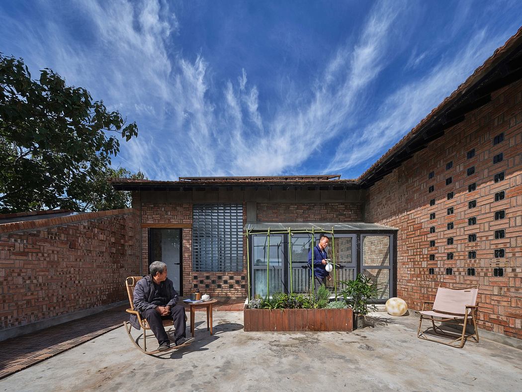 Brick house with patio, two people, chairs, and potted plants under