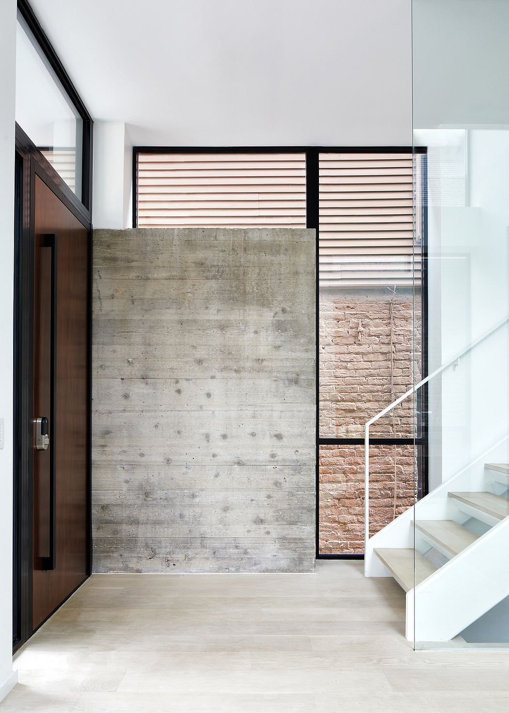 Modern hallway with concrete wall, wooden door, and glass staircase.