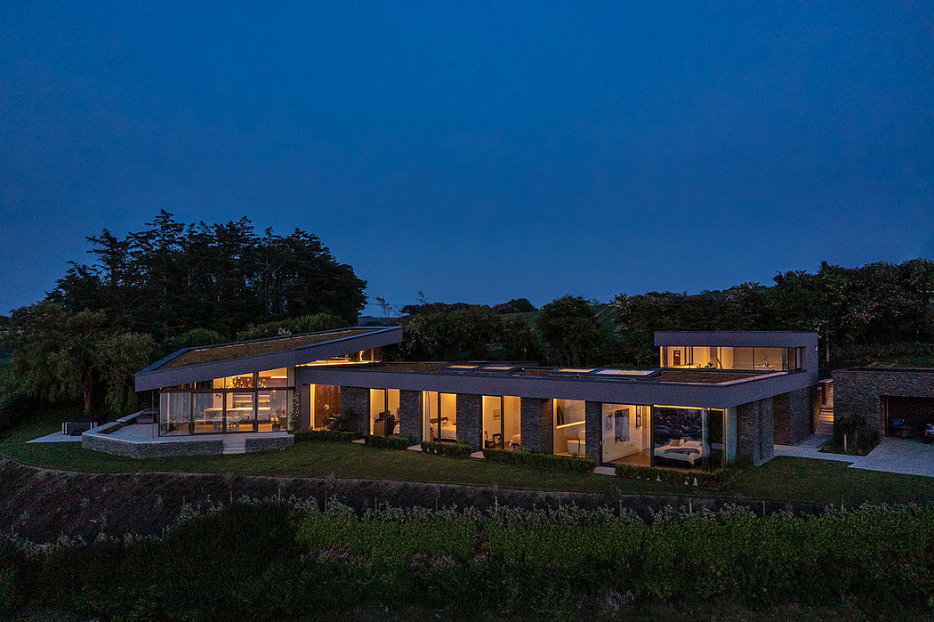 Single-story house with illuminated interiors at twilight surrounded by trees.