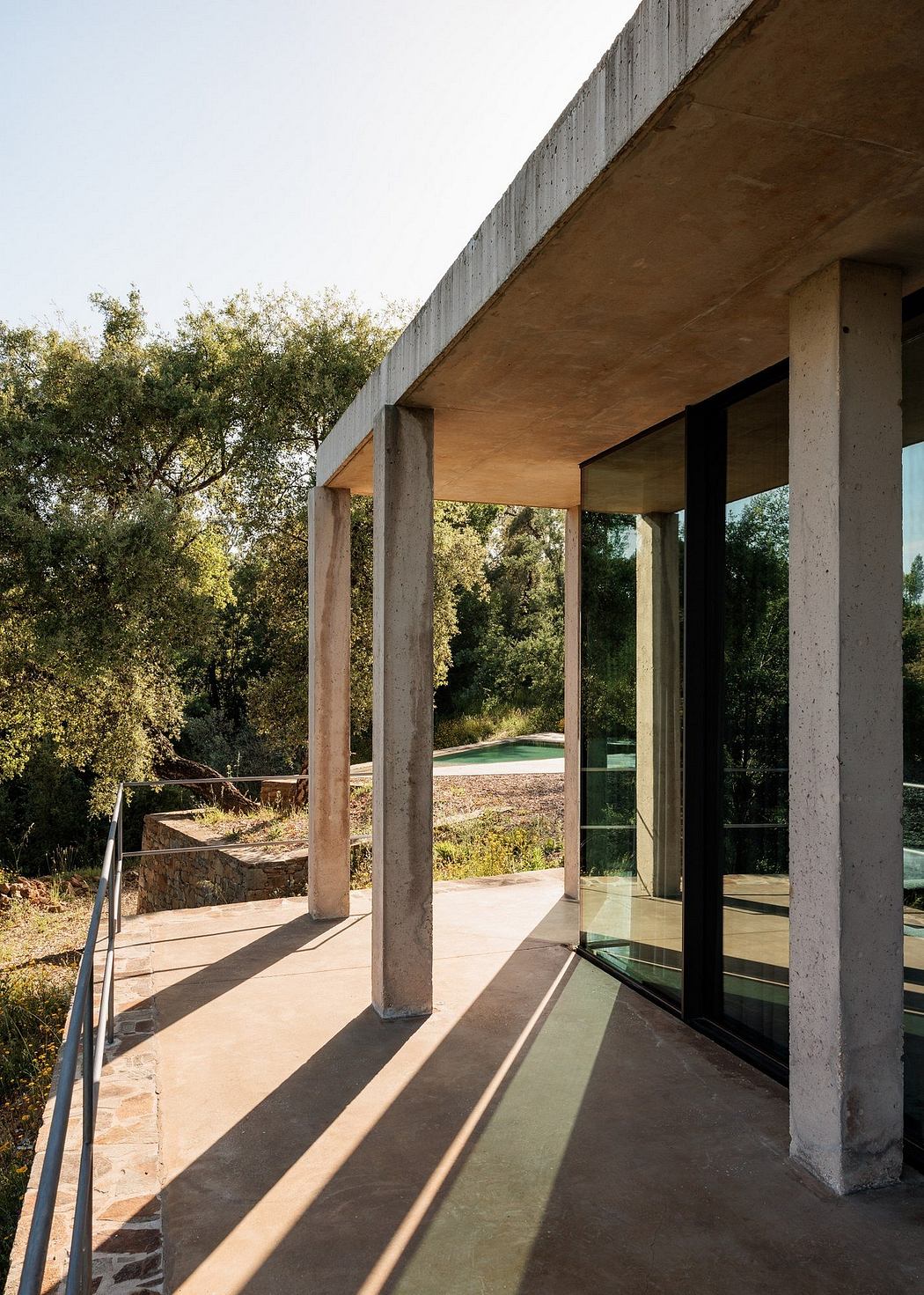 Modern terrace with concrete pillars and glass doors overlooking greenery.