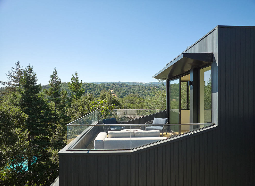 Contemporary home terrace with a glass balustrade overlooking a forest.