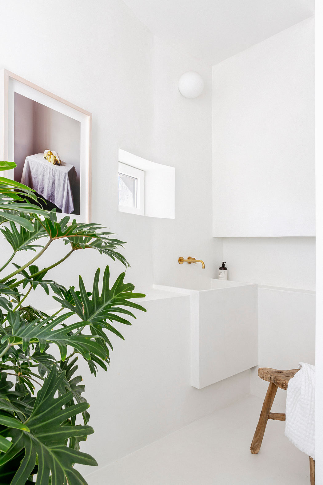 Minimalist white bathroom with green plant and wooden stool.