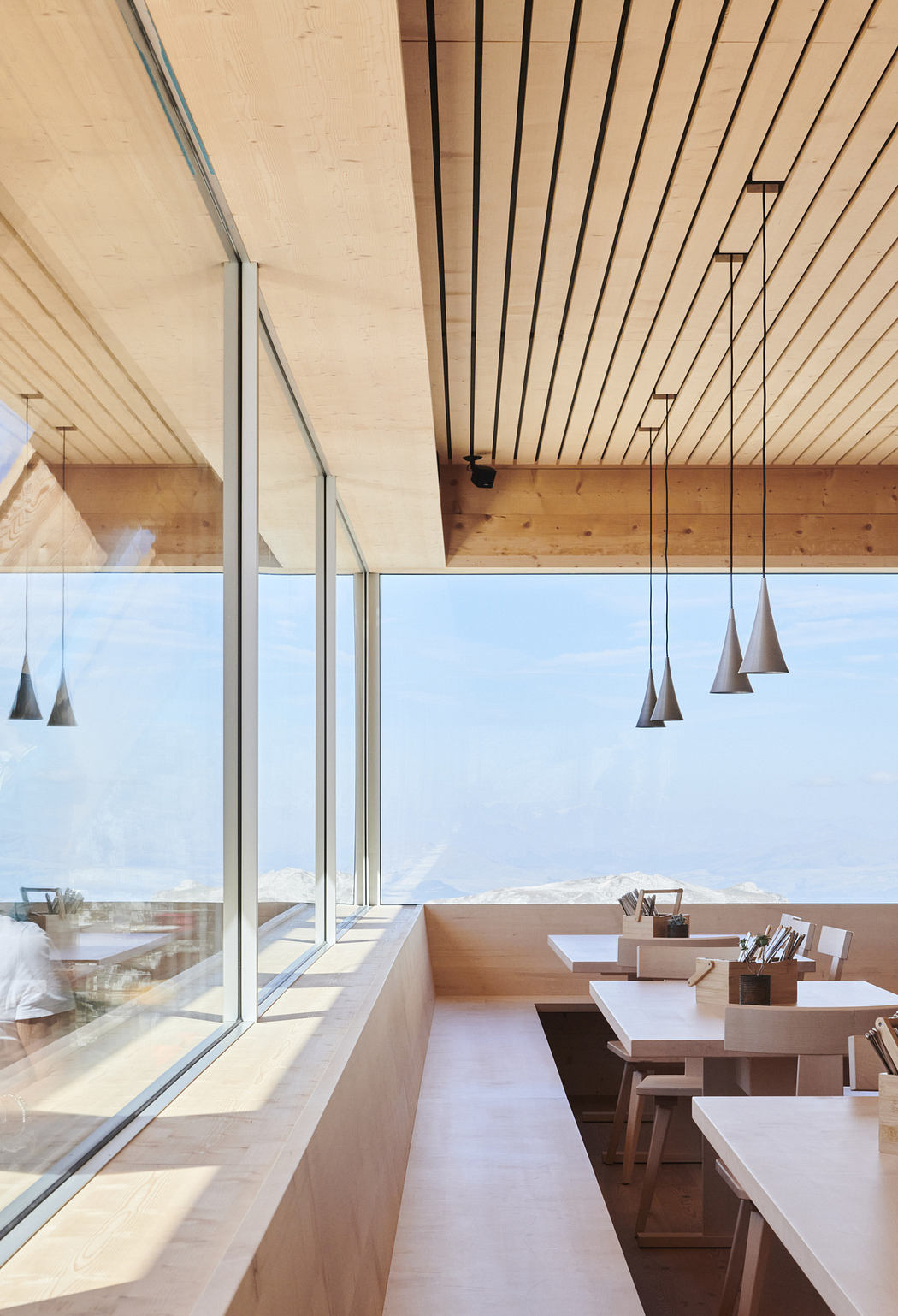 Bright, wooden interior with floor-to-ceiling windows and pendant lights.