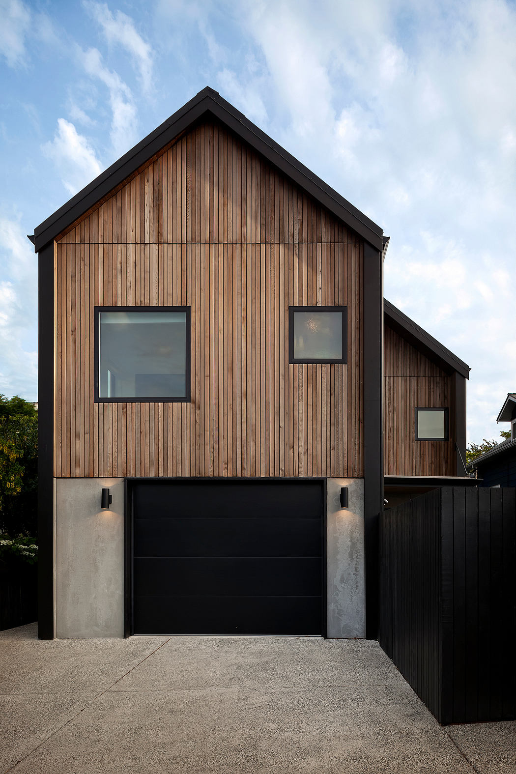 Contemporary wooden-clad home with a slanted roof and black garage.