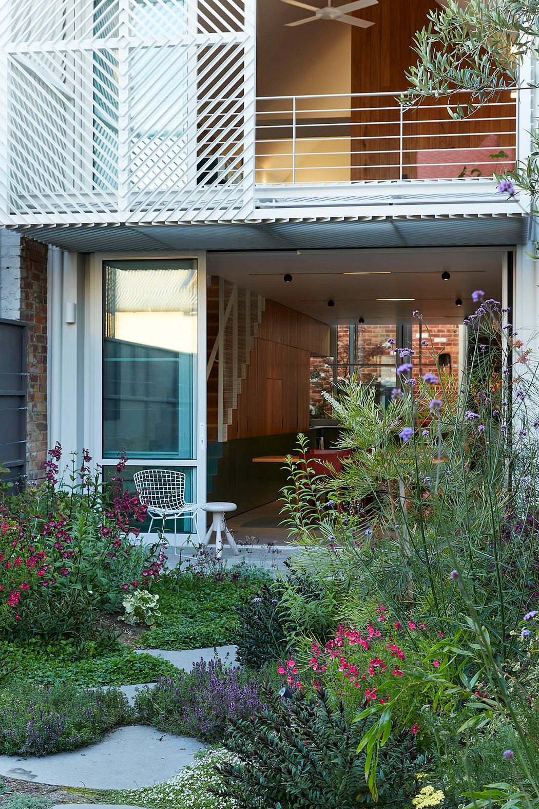 Contemporary home with garden, featuring a geometric balcony and warm interior lighting.