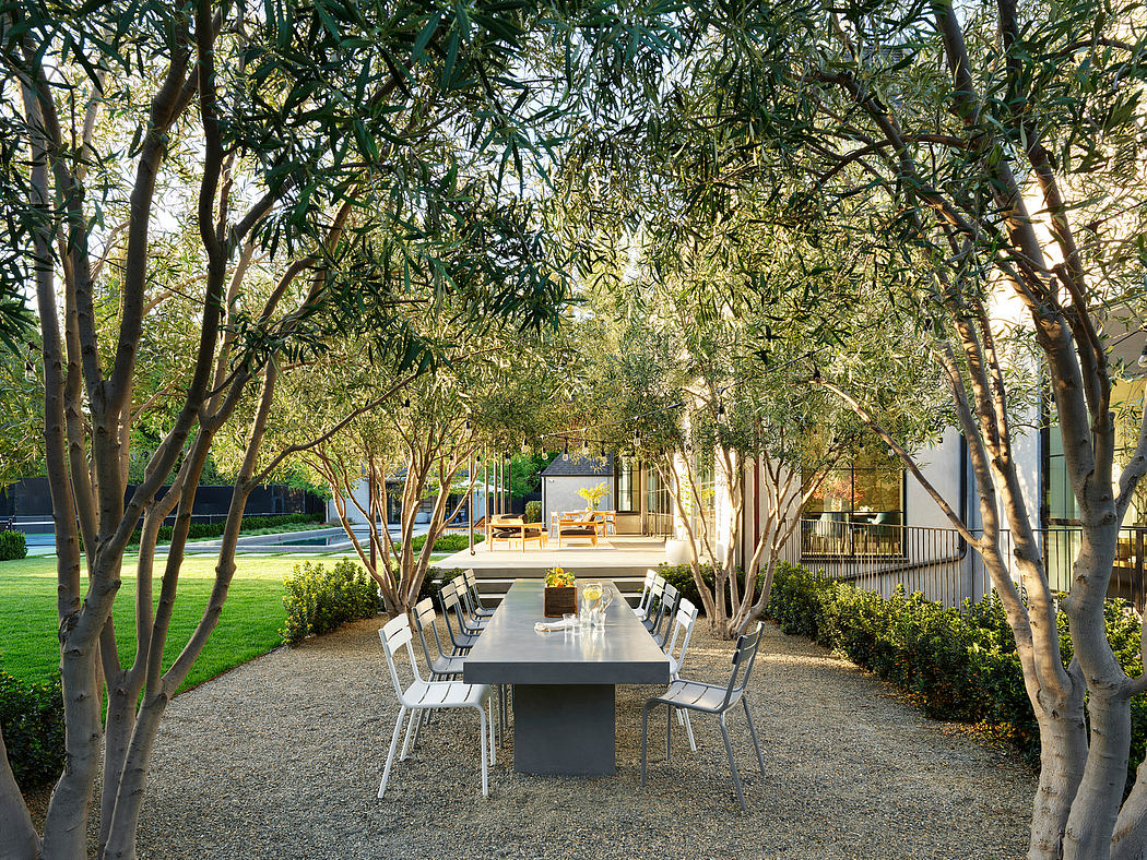 Outdoor dining area with table and chairs surrounded by trees and hedges.