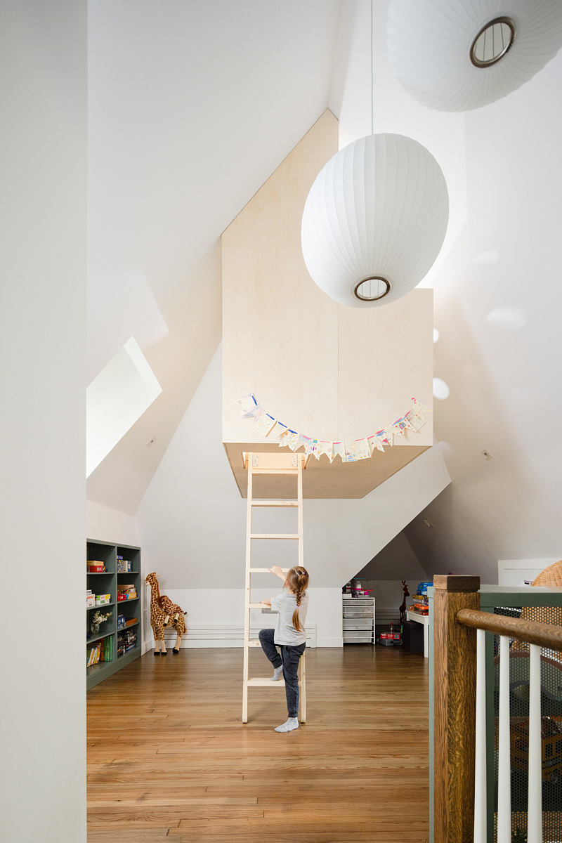 Minimalist interior with a child looking at a wooden loft accessed by a white ladder