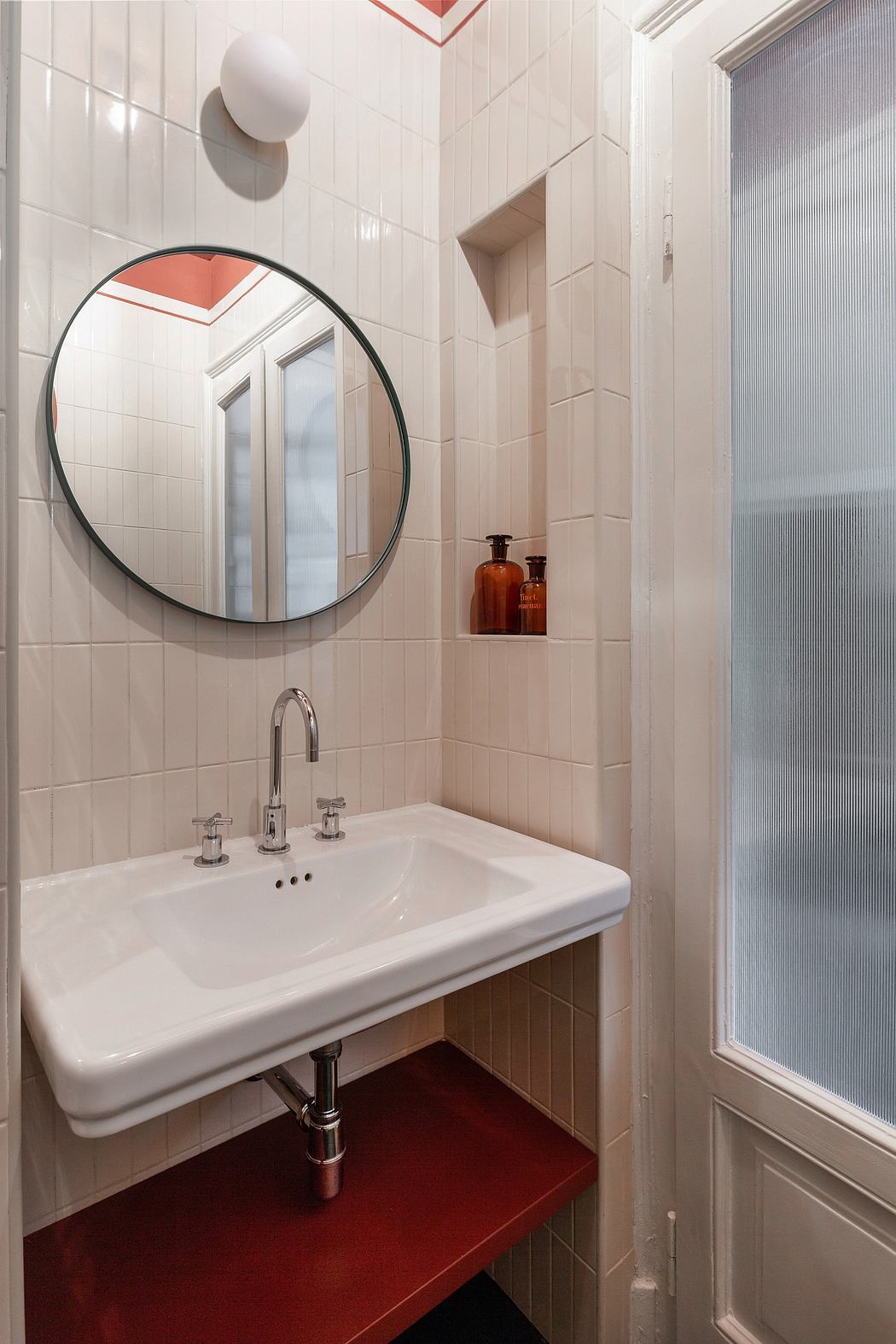 Small bathroom with white sink, circular mirror, and tiled walls.