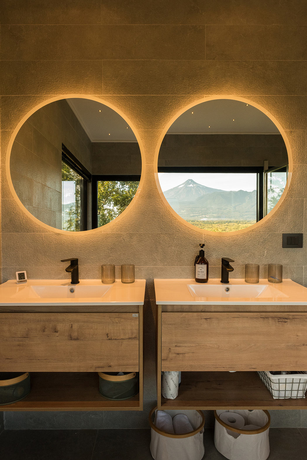 A modern bathroom with twin sinks and circular mirrors showcasing a mountain view.