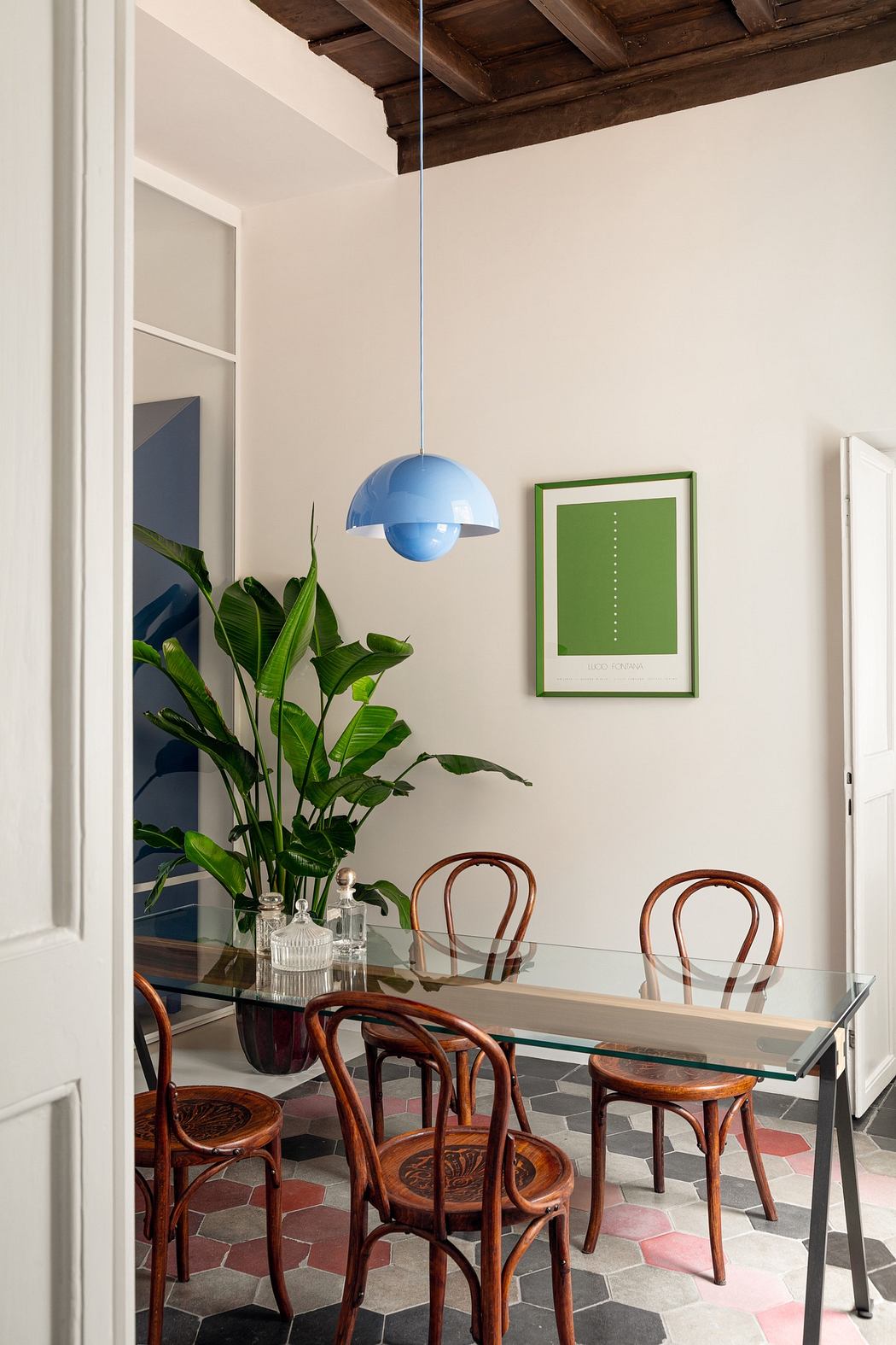 Modern dining room with glass table, bentwood chairs, blue pendant light, and