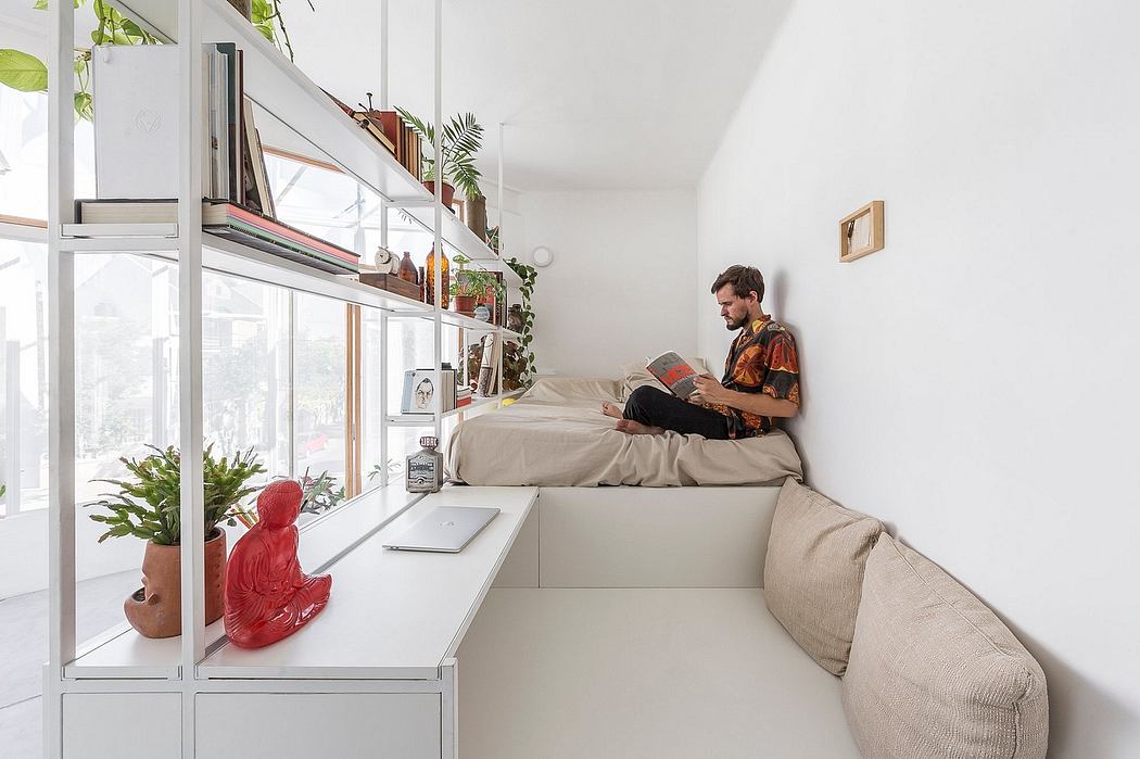 Man reading on a cushioned windowsill bench in a modern, plant-filled room