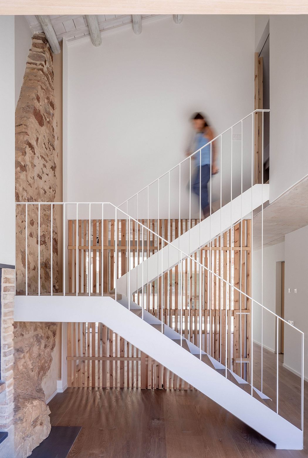 Modern staircase with wooden steps, white railing, and a blurred person ascending.