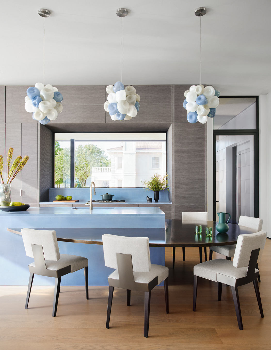 Modern kitchen with blue island, dining table, unique pendant lights, and neutral tones