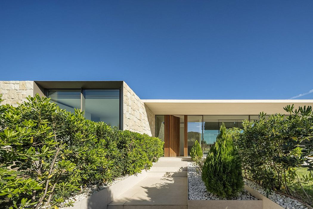 Contemporary house entrance with stone walls and large windows flanked by lush greenery