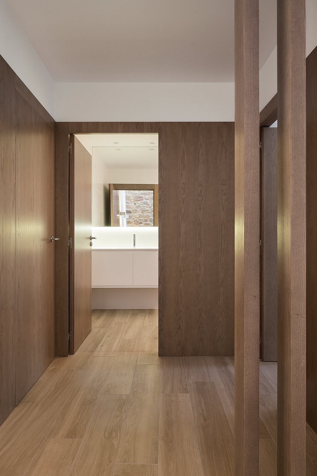 Modern hallway with wooden doors and flooring leading to a bright room.