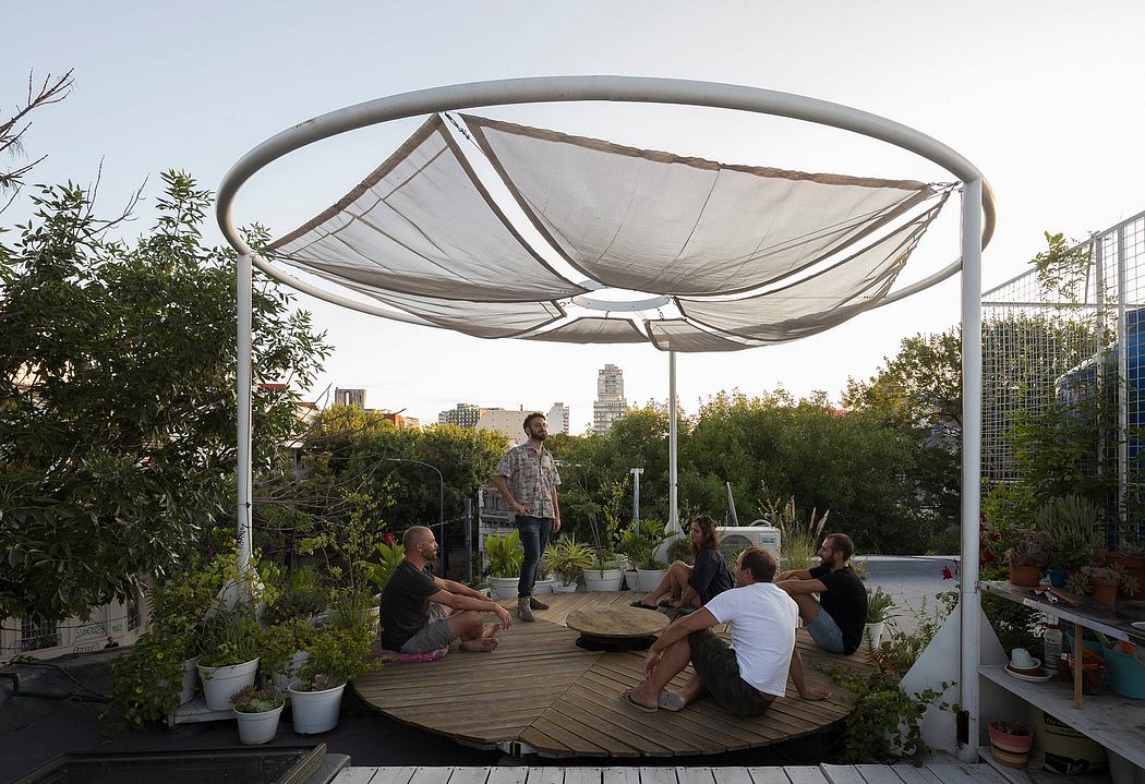 Urban rooftop gathering with a circular shaded seating area and potted plants.