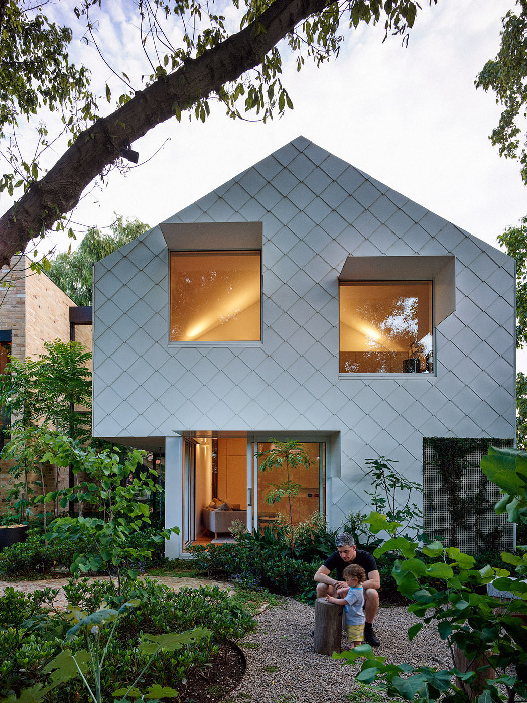 Contemporary house with geometric facade and illuminated windows, family in foreground.
