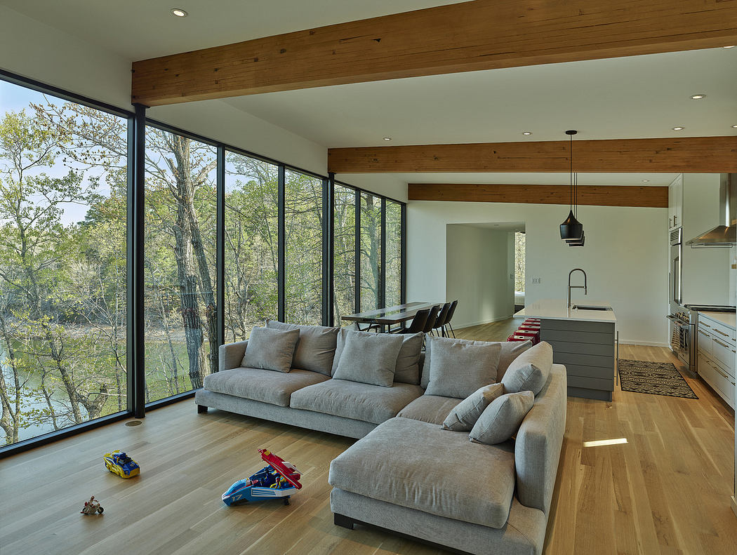 Modern living room with large windows, sectional sofa, and wooden beams.