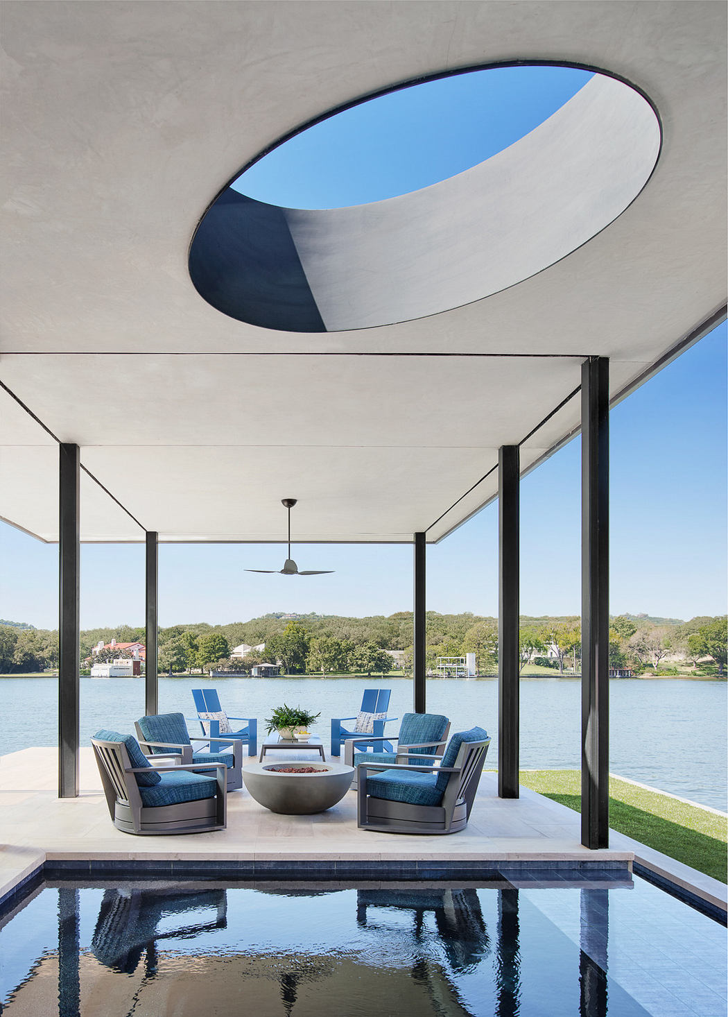 Modern lakeside patio with oval ceiling cutout, sleek furniture, and reflective water