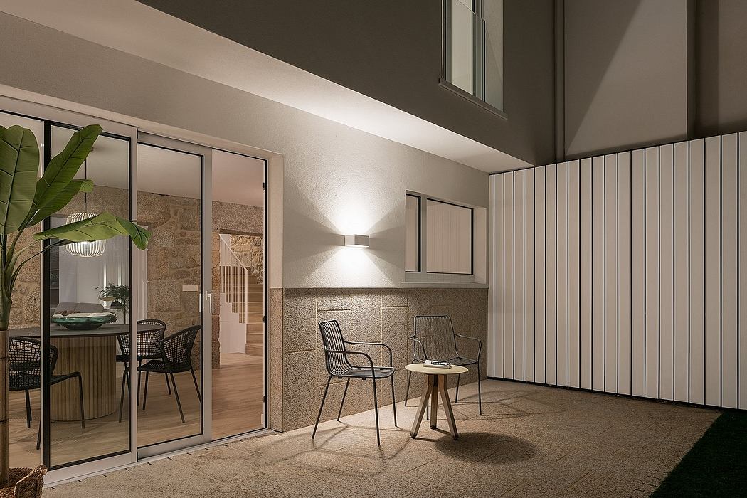 Modern patio with chairs, table, and sliding glass doors at night.