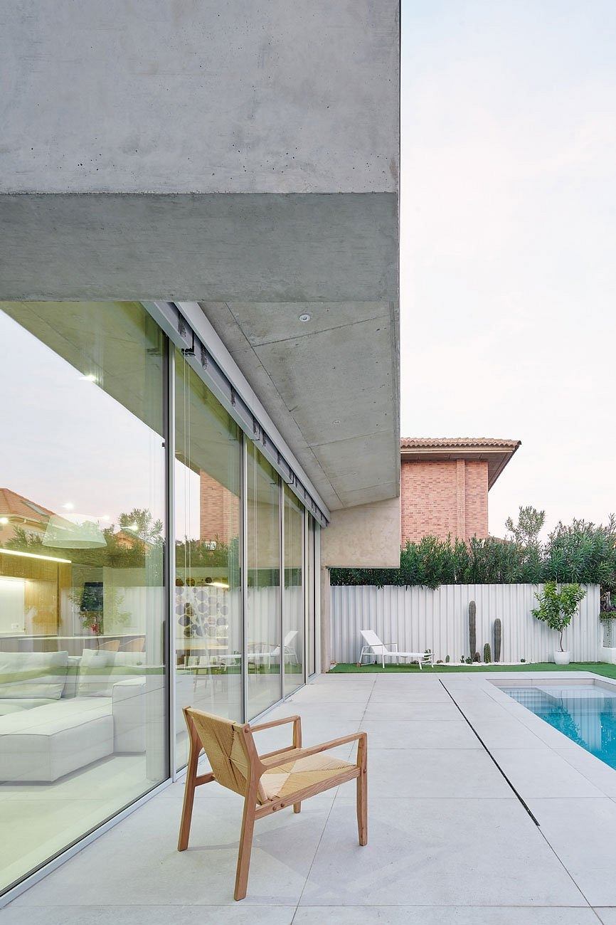 Modern home exterior with concrete, glass walls, and a wooden chair by a pool