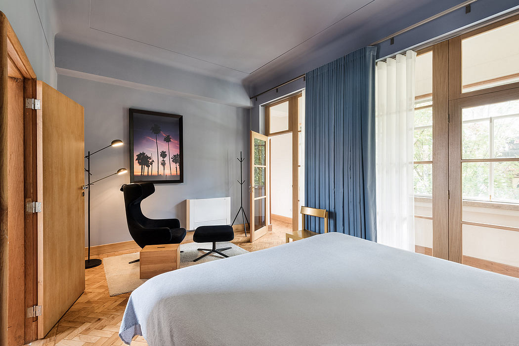 Contemporary bedroom with blue drapes, wood flooring, and stylish chair.