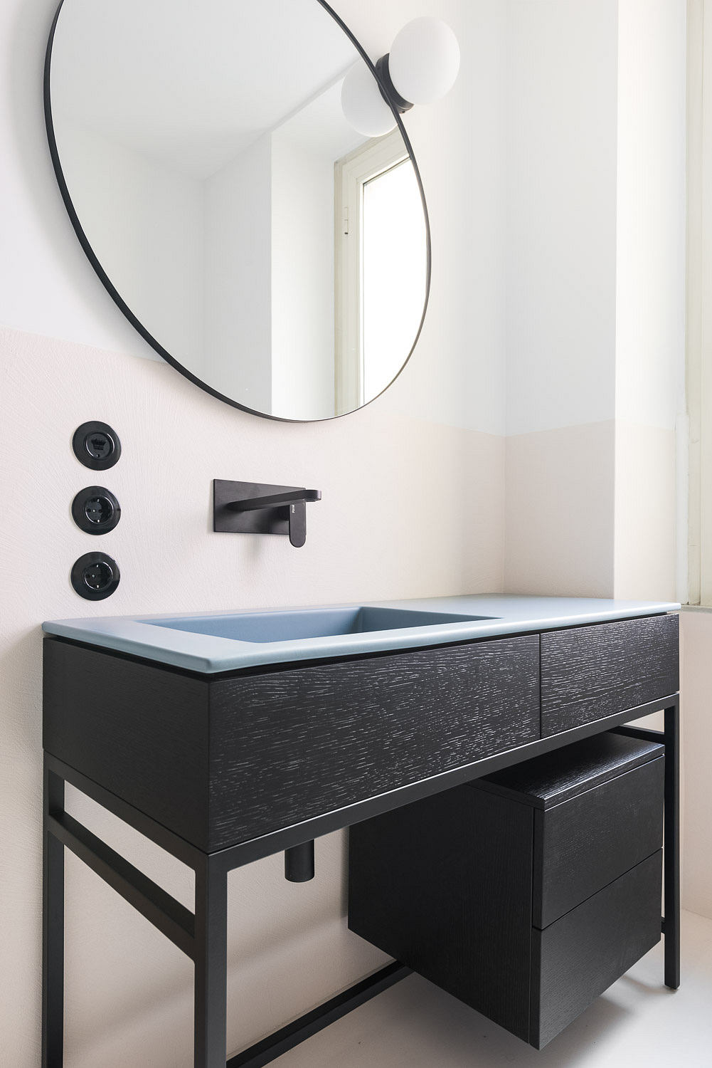 Minimalist bathroom vanity with sleek black fixtures and a circular mirror.