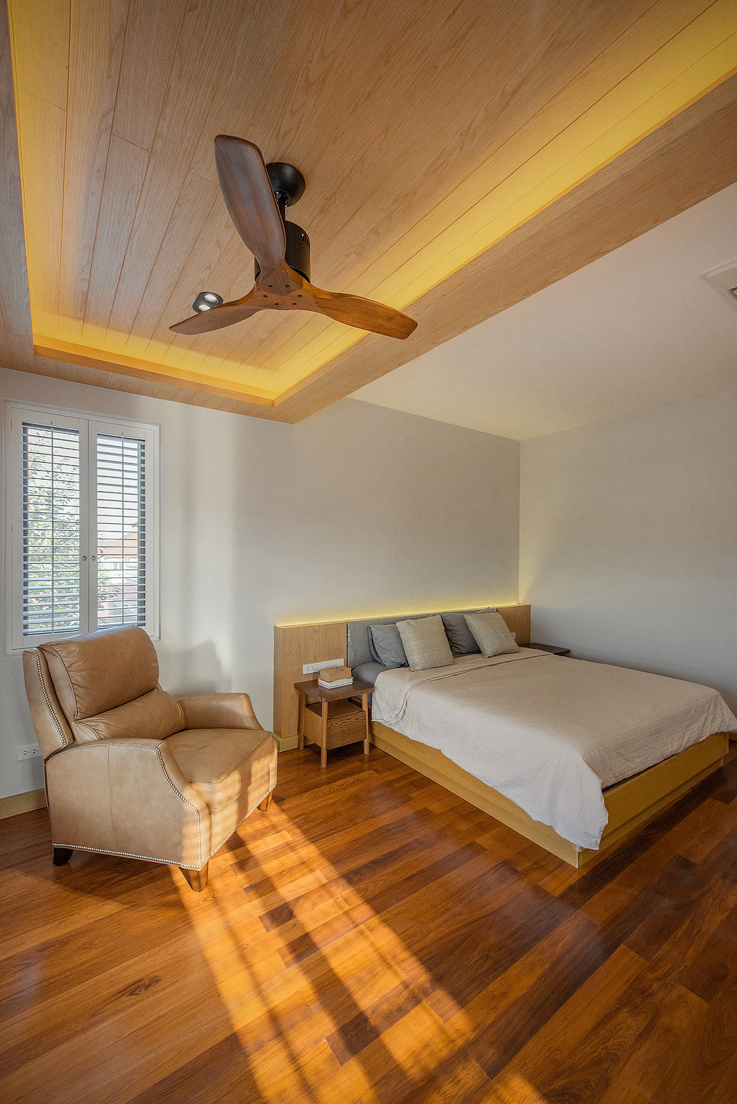 Contemporary bedroom with wooden floors, ceiling fan, and sunlit ambiance.