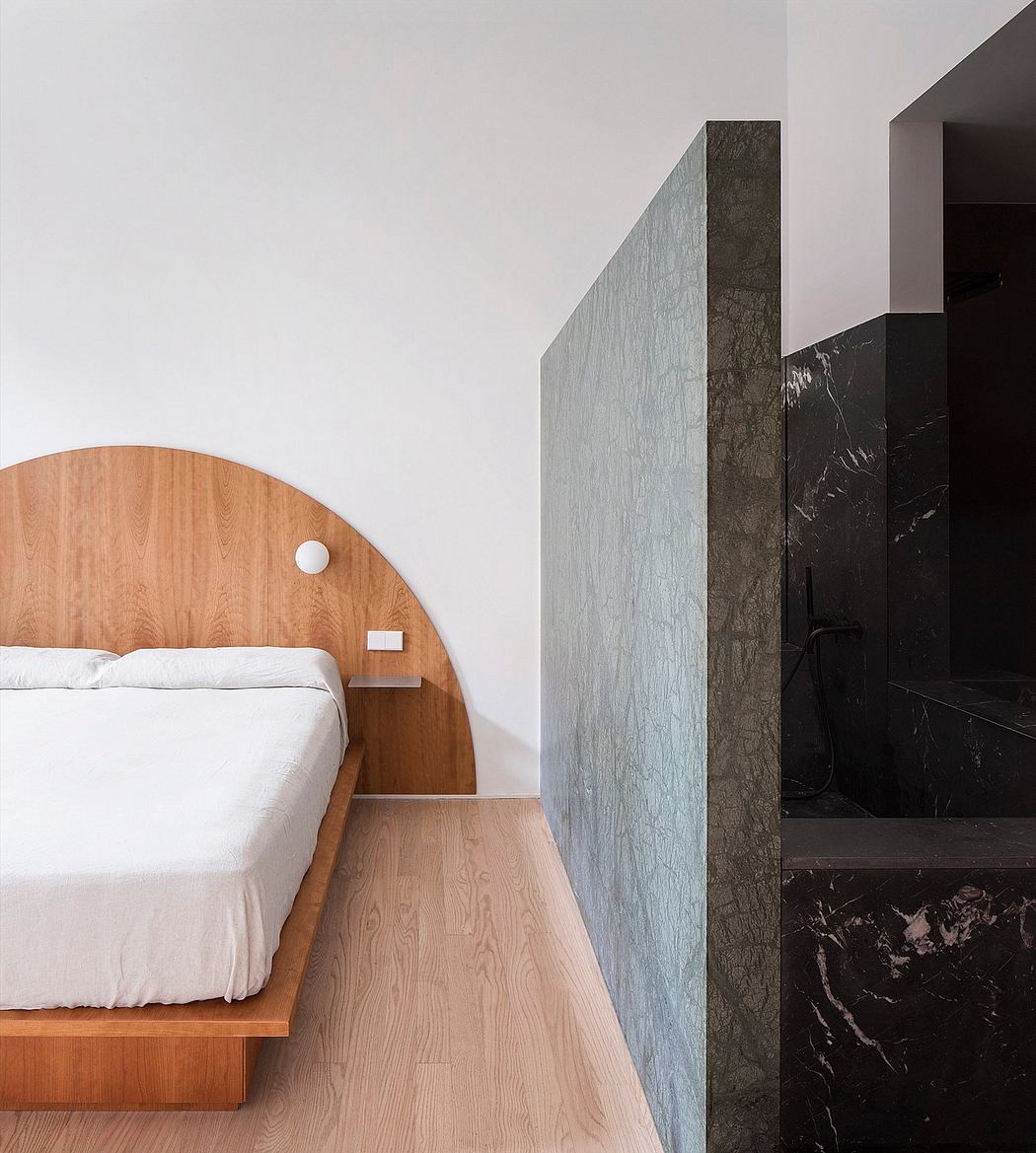 Minimalist bedroom with wooden bed and partial stone wall divider.