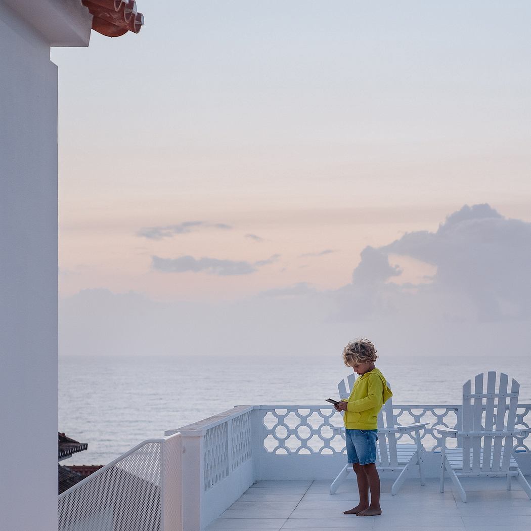 Child on a seaside balcony at dusk with an expansive view of the ocean.