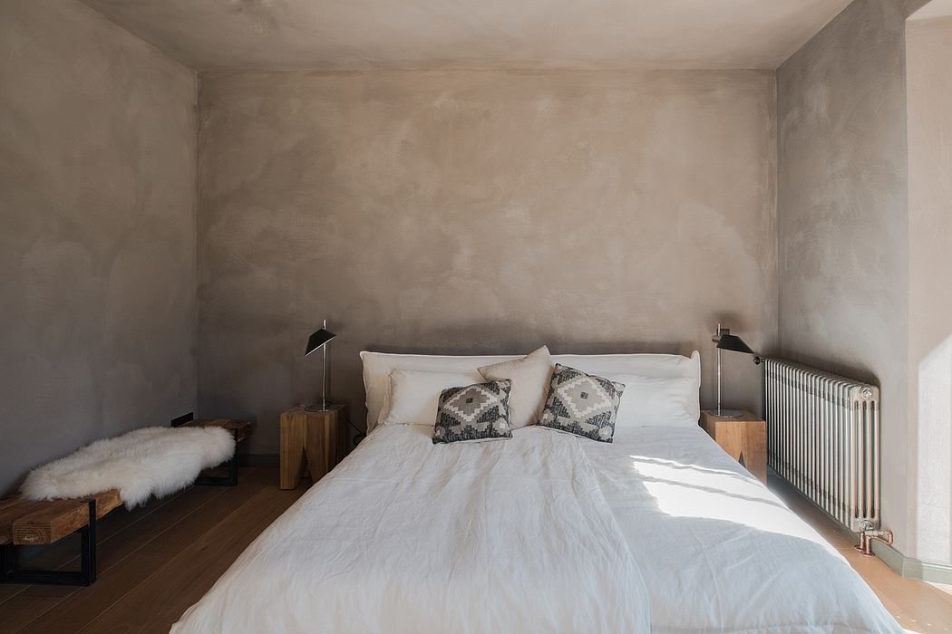 Minimalist bedroom with a white bed, concrete walls, and wooden furnishings.