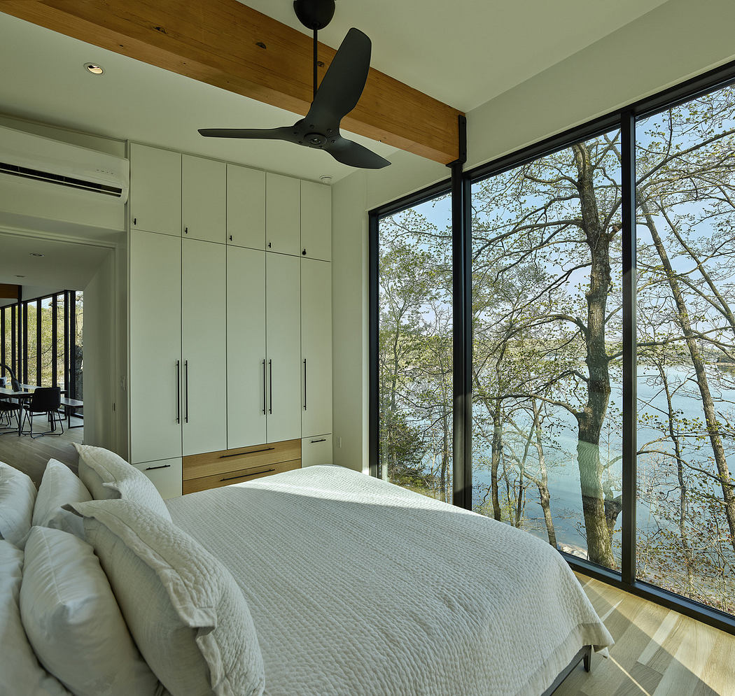 Modern bedroom with floor-to-ceiling windows overlooking a lake.