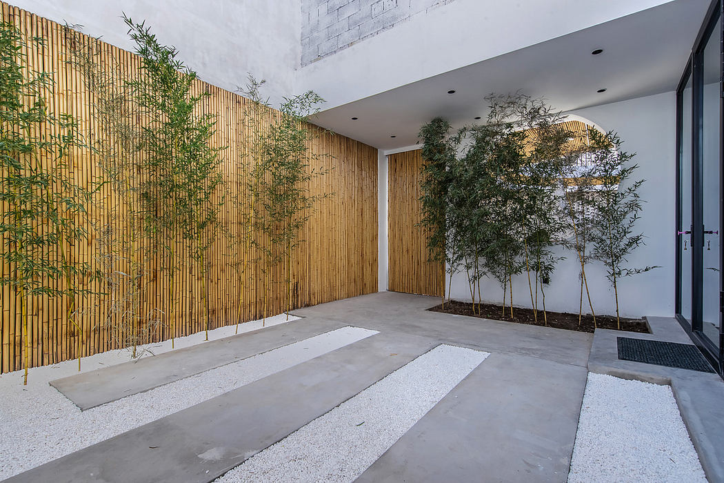 Modern courtyard with bamboo fencing, stepping stones, and potted plants.