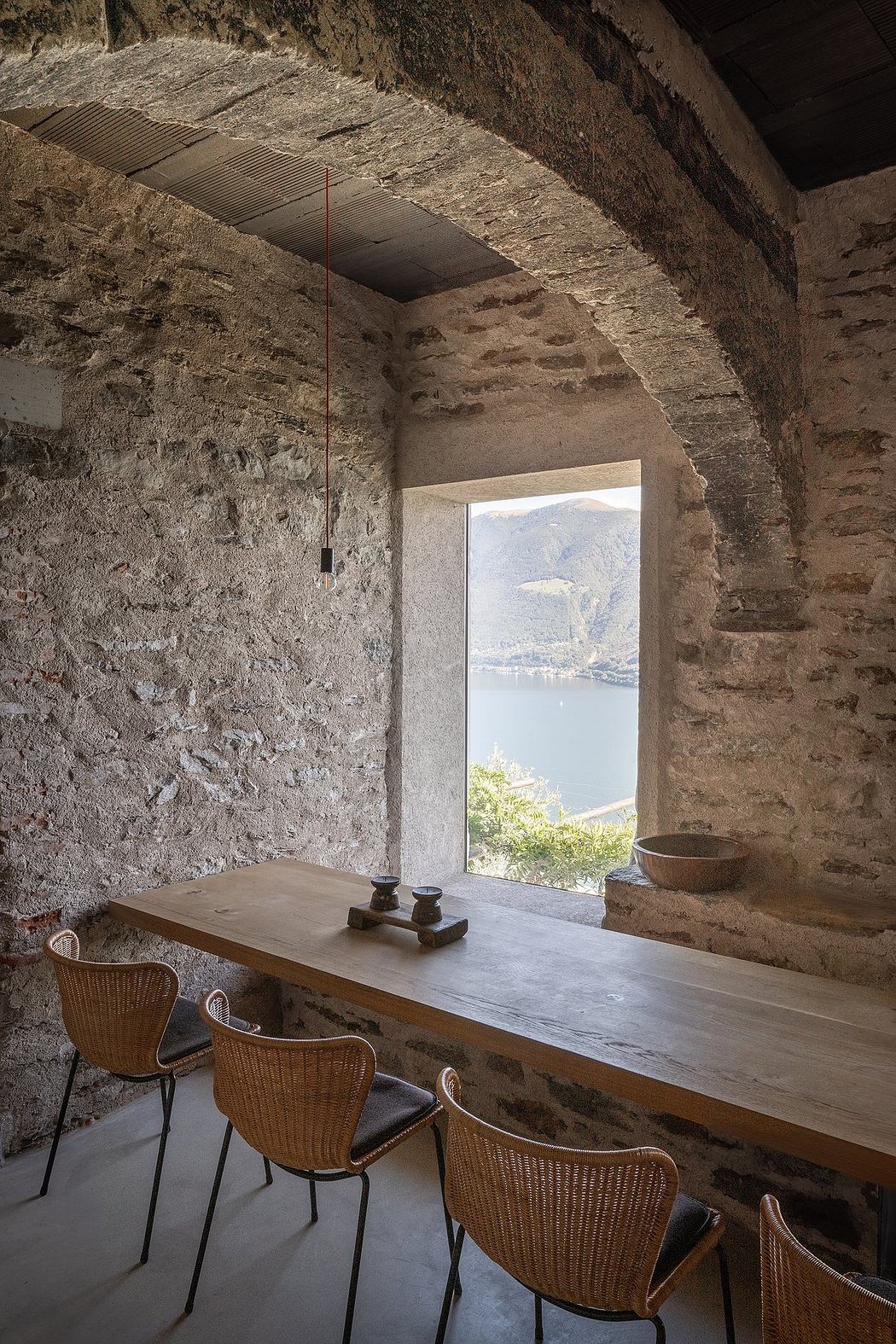 Rustic dining space with stone walls and archway overlooking a lake.