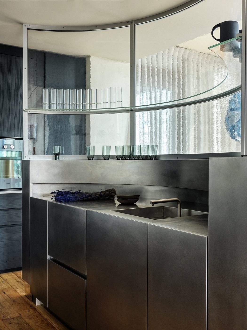 Contemporary kitchen with stainless steel cabinets and curved glass shelving.