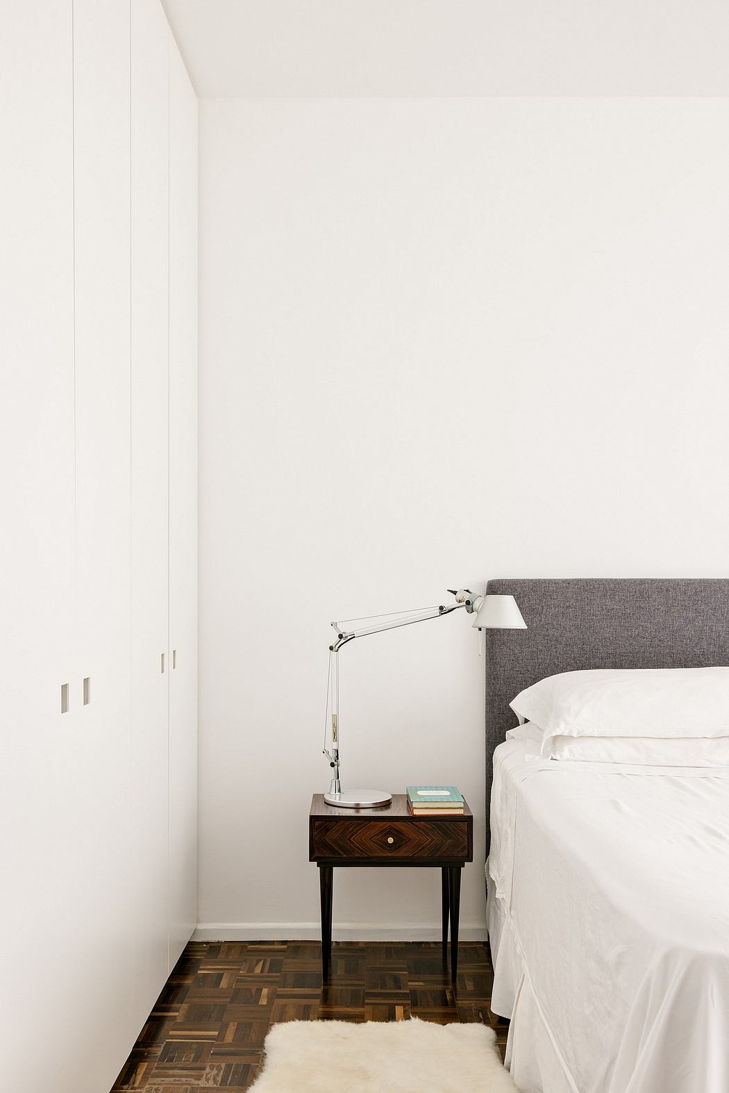 Minimalist bedroom with white walls, a bedside table, lamp, and part of
