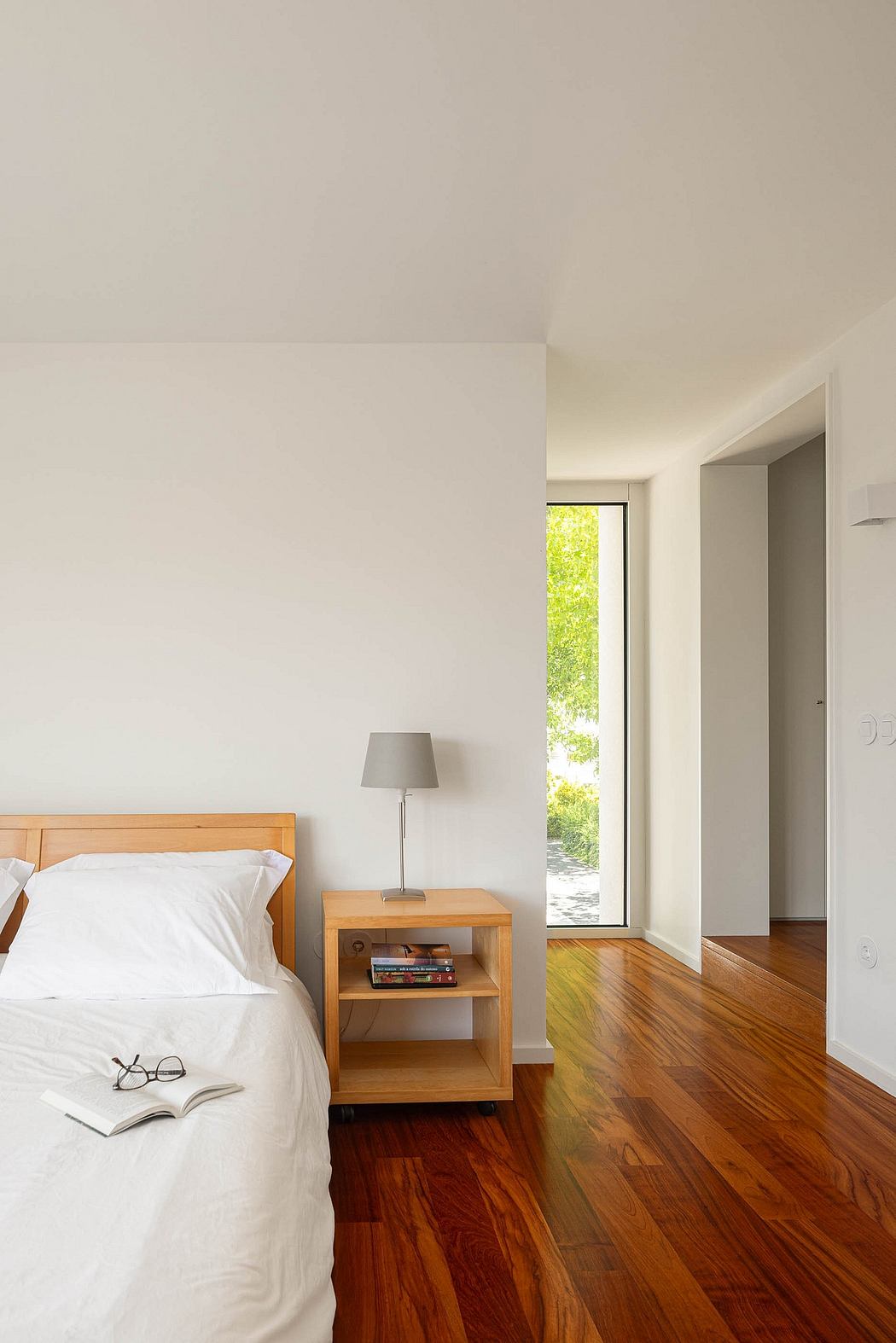 Minimalist bedroom with a wooden bed, side table, lamp, and polished hardwood