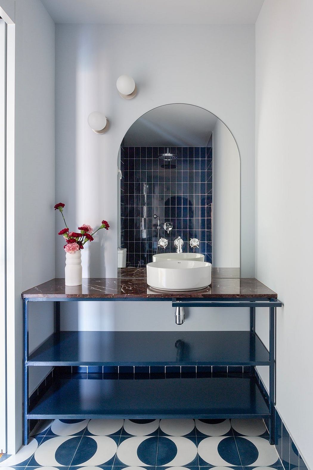 Modern bathroom nook with arched mirror, navy blue tiles, and patterned