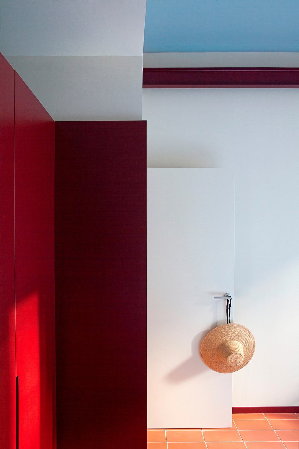 Minimalist interior with red column, white walls, blue trim, and a hanging