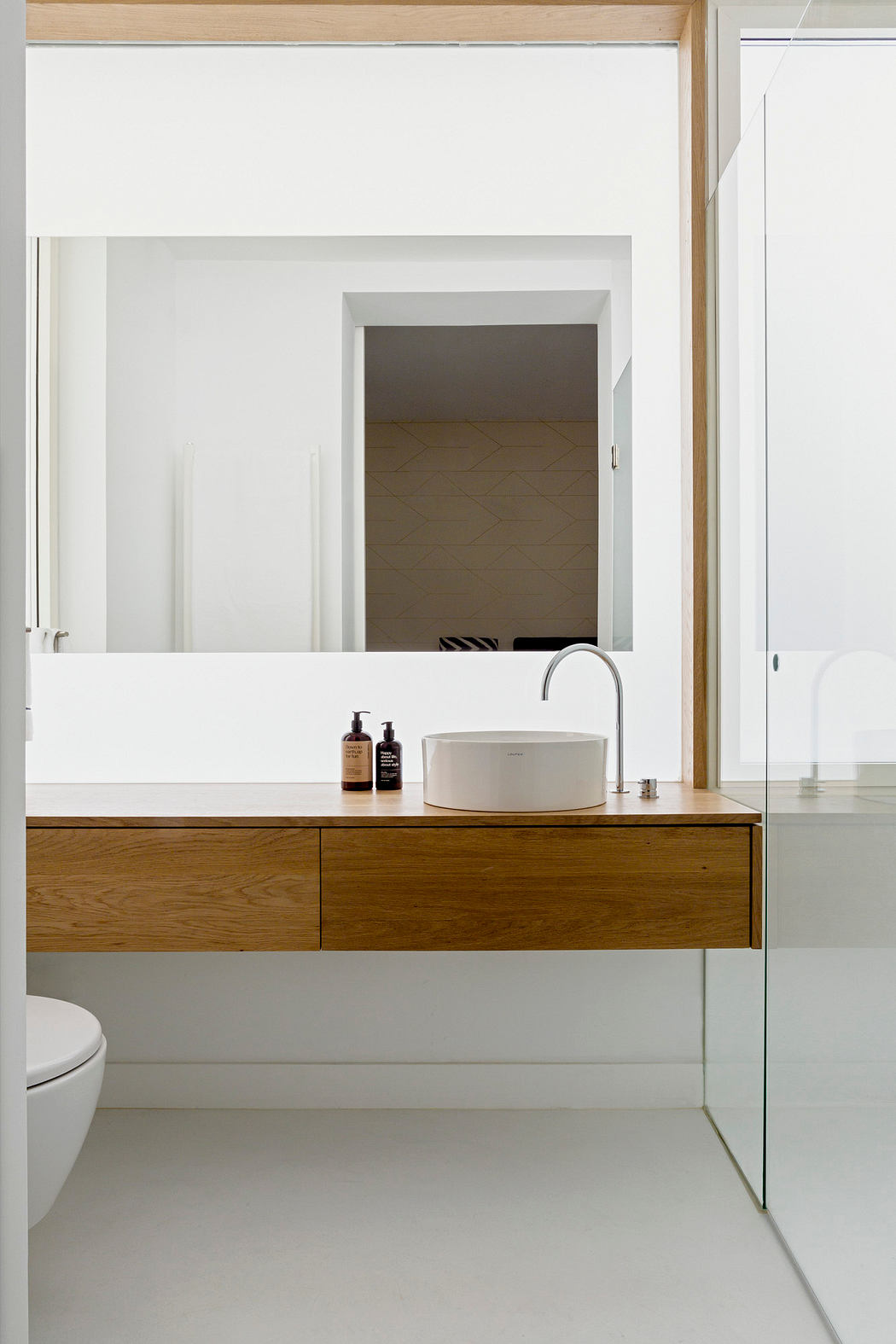 Modern bathroom with wooden vanity, white basin, mirror, and toilet.
