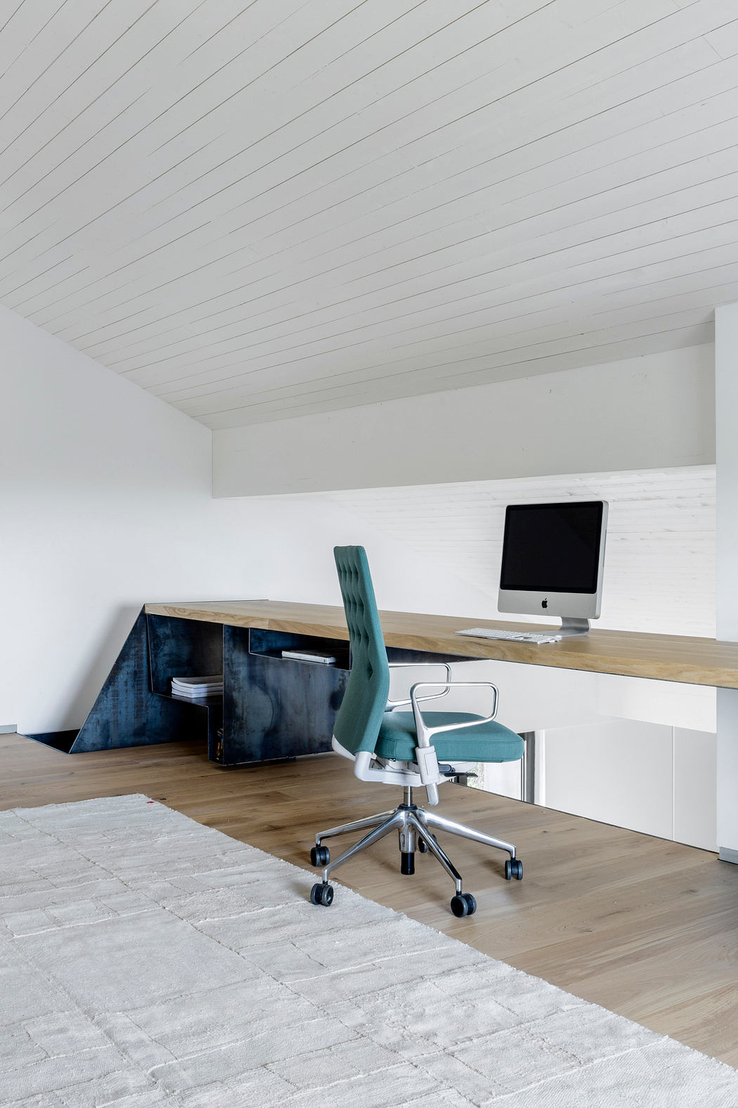 Minimalist home office with white walls, slanted ceiling, and wooden flooring.