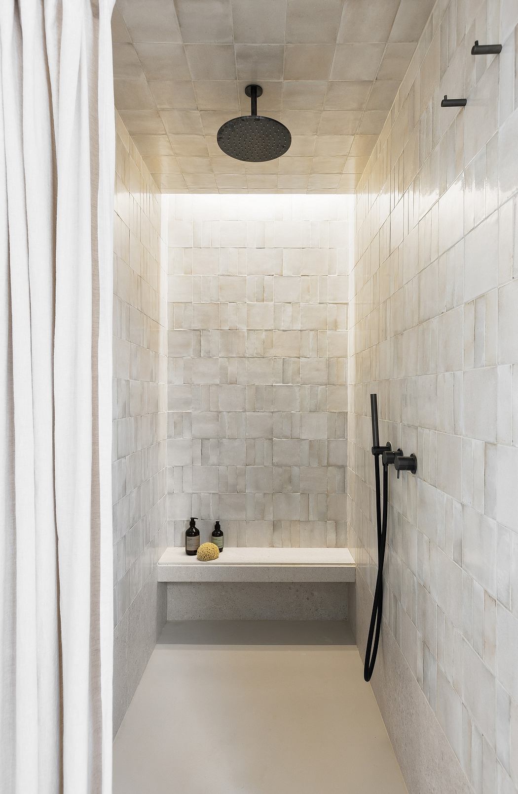 Minimalistic white-tiled walk-in shower with black fixtures.